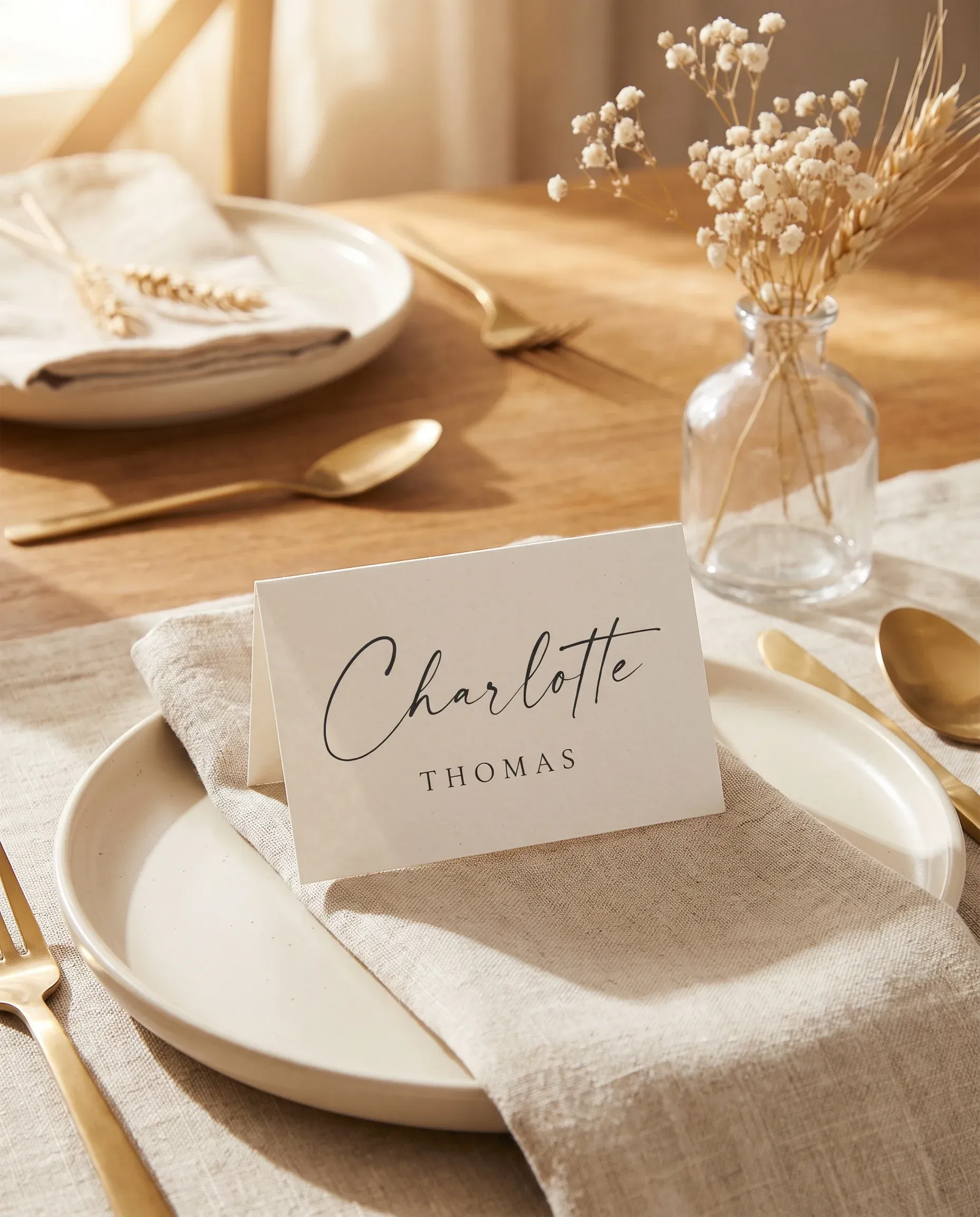 Sunlit wedding place cards — a single card resting at a table setting under soft overhead light, wedding name cards.